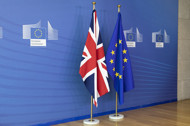 na niebieskim tle stojak z dwiema flagami - z lewej flaga Wielkiej Brytanii a z prawej Unii Europejskiej